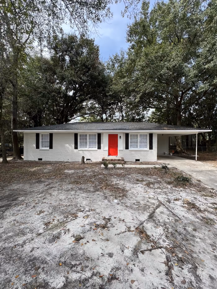 Renovated white brick ranch home with bright red front door under oak trees in Georgia