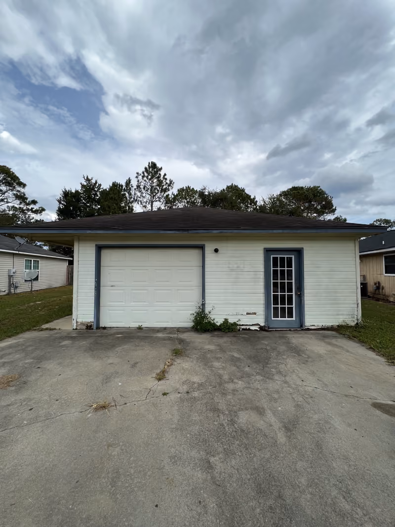 Small white house with garage-front entrance and cracked driveway, purchased as-is in Georgia