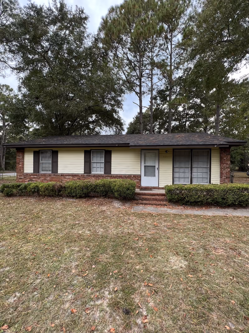 Small yellow and brick ranch house with hedges bought as-is in Georgia